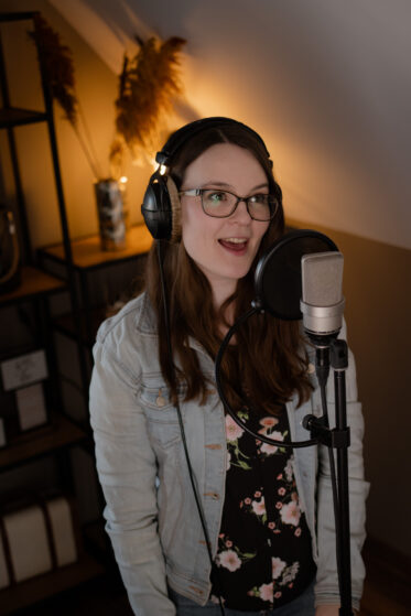 Hannah Stienen steht mit Kopfhörern auf vor einem Mikrofon und singt. Man könnte meinen, sie nimmt (Demo)Gesangsspuren für ein persönliches Lied auf.