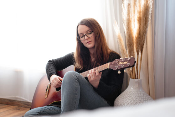 Hannah Stienen sitzt auf dem Boden mit ihrer Gitarre und probiert Ideen für einen persönlichen Song aus.