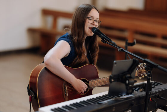 Hannah Stienen steht mit ihrer Gitarre in einer Kirche und singt.
