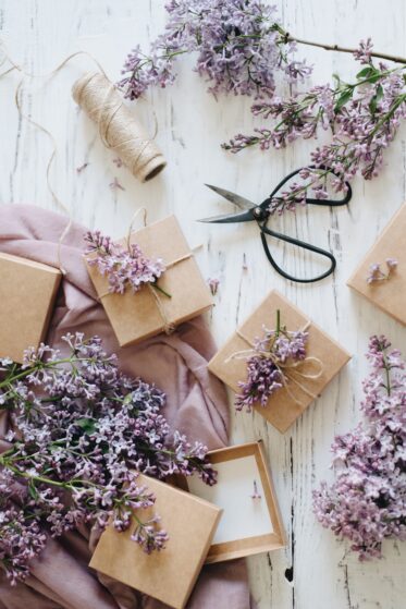 Flatlay: In braunem Papier verpackte Geschenke liegen auf dem Boden. Lavendel, Band und eine Schere liegen dazwischen.