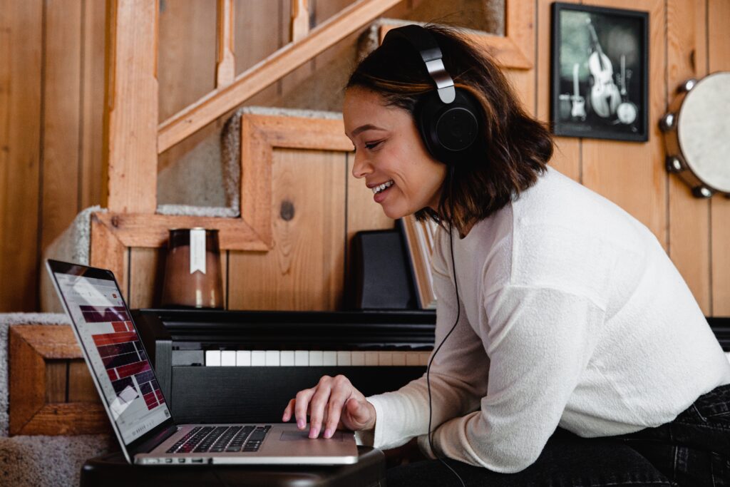 Eine Frau sitzt mit Kopfhörern auf vor ihrem Laptop. Sie könnte einen Song produzieren.